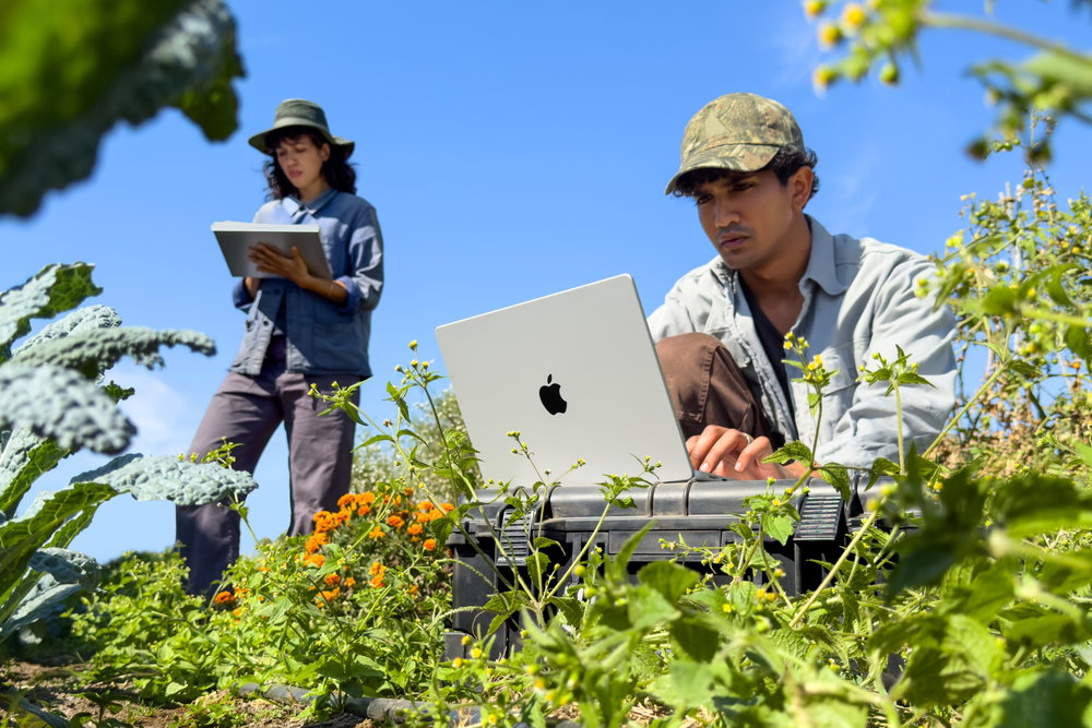 Twee mensen gebruiken een MacBook Pro tijdens veldwerk in de buitenlucht.